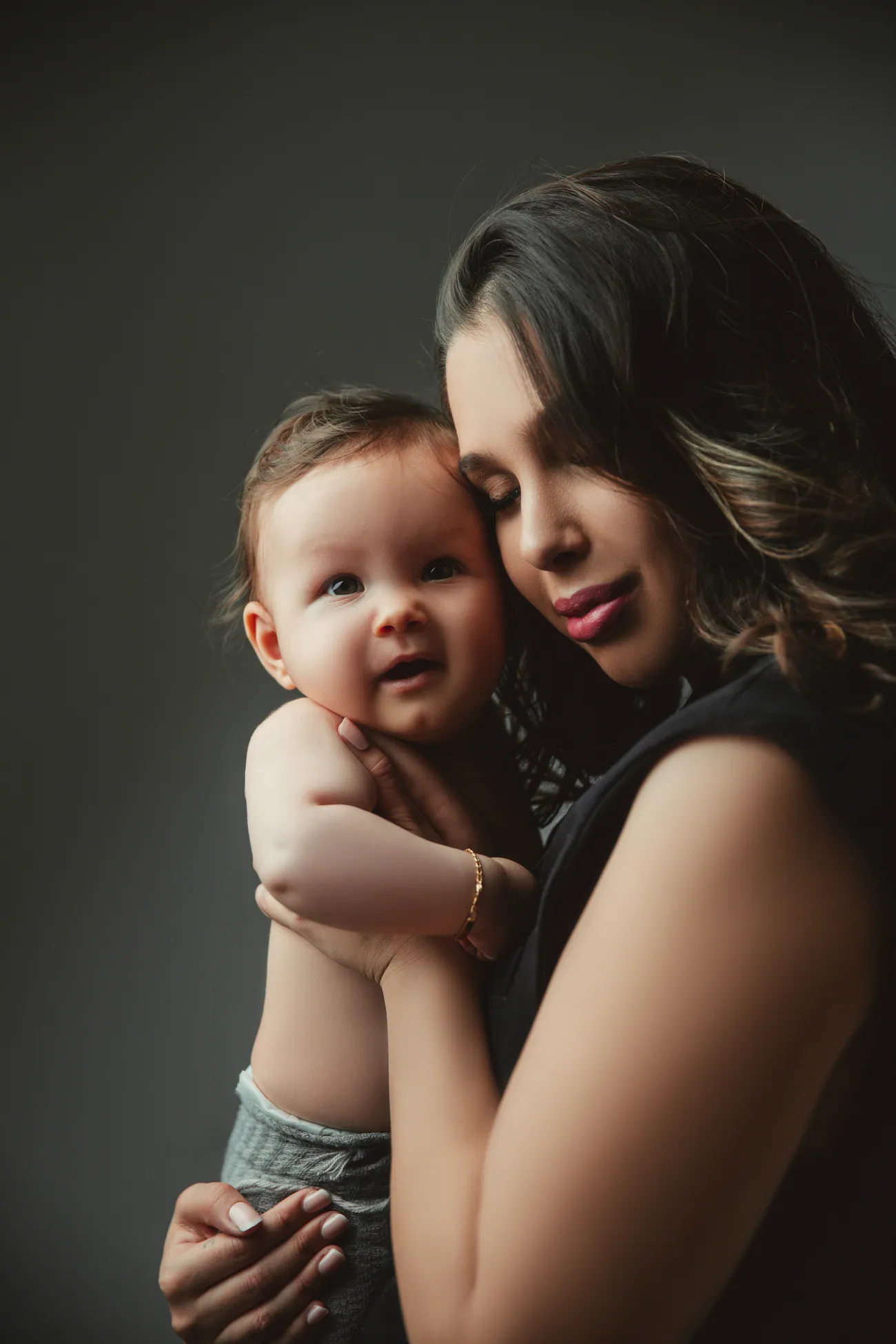 Mutter mit Kleinkind vor dunklem Hintergrund, warmes Familienportrait.