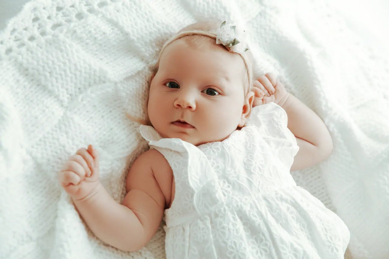 Baby auf einer weißen Decke, fröhlicher Blick in die Kamera.