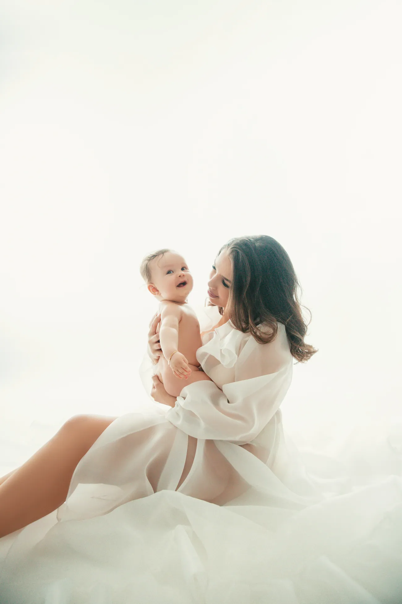 Mutter und Baby in fließendem weißem Stoff, ätherisches, helles Bild.