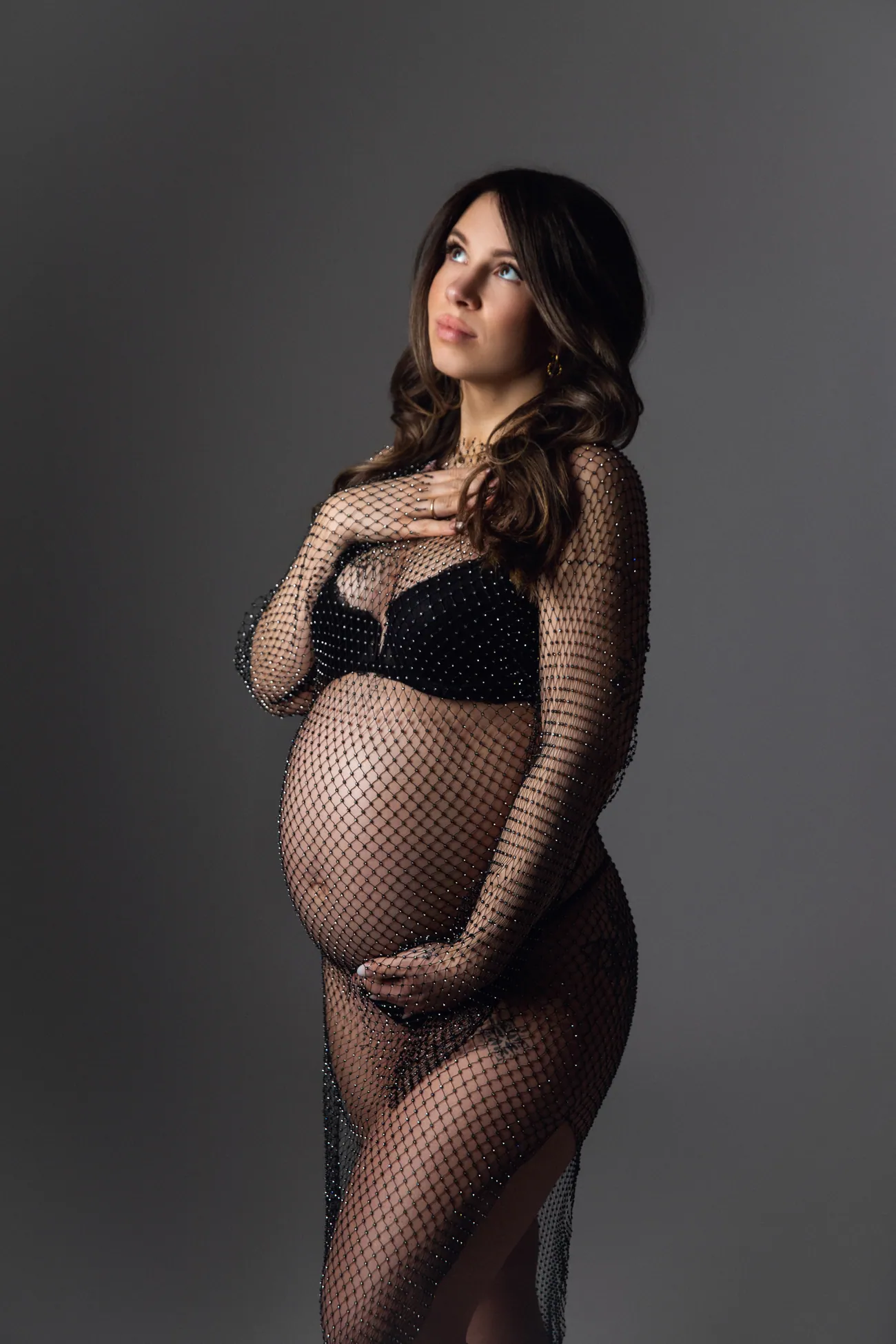 Elegantes Babybauch-Portrait vor grauem Studiohintergrund.