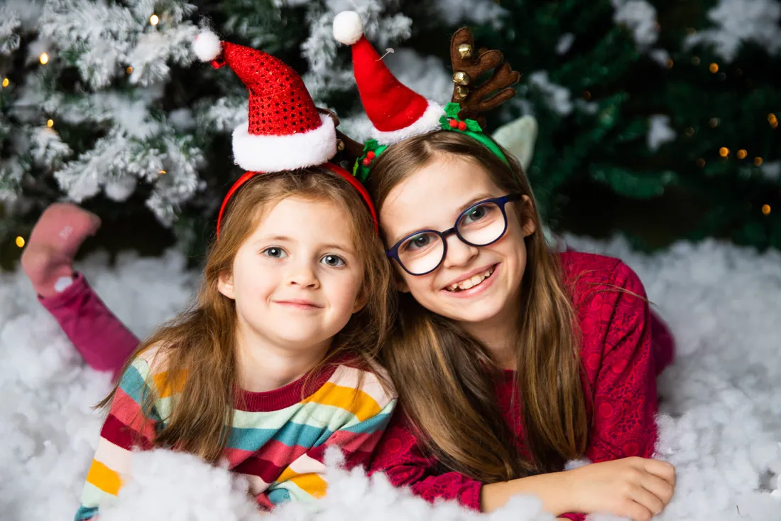 Zwei Kinder mit Weihnachtsmützen vor winterlichem Hintergrund.