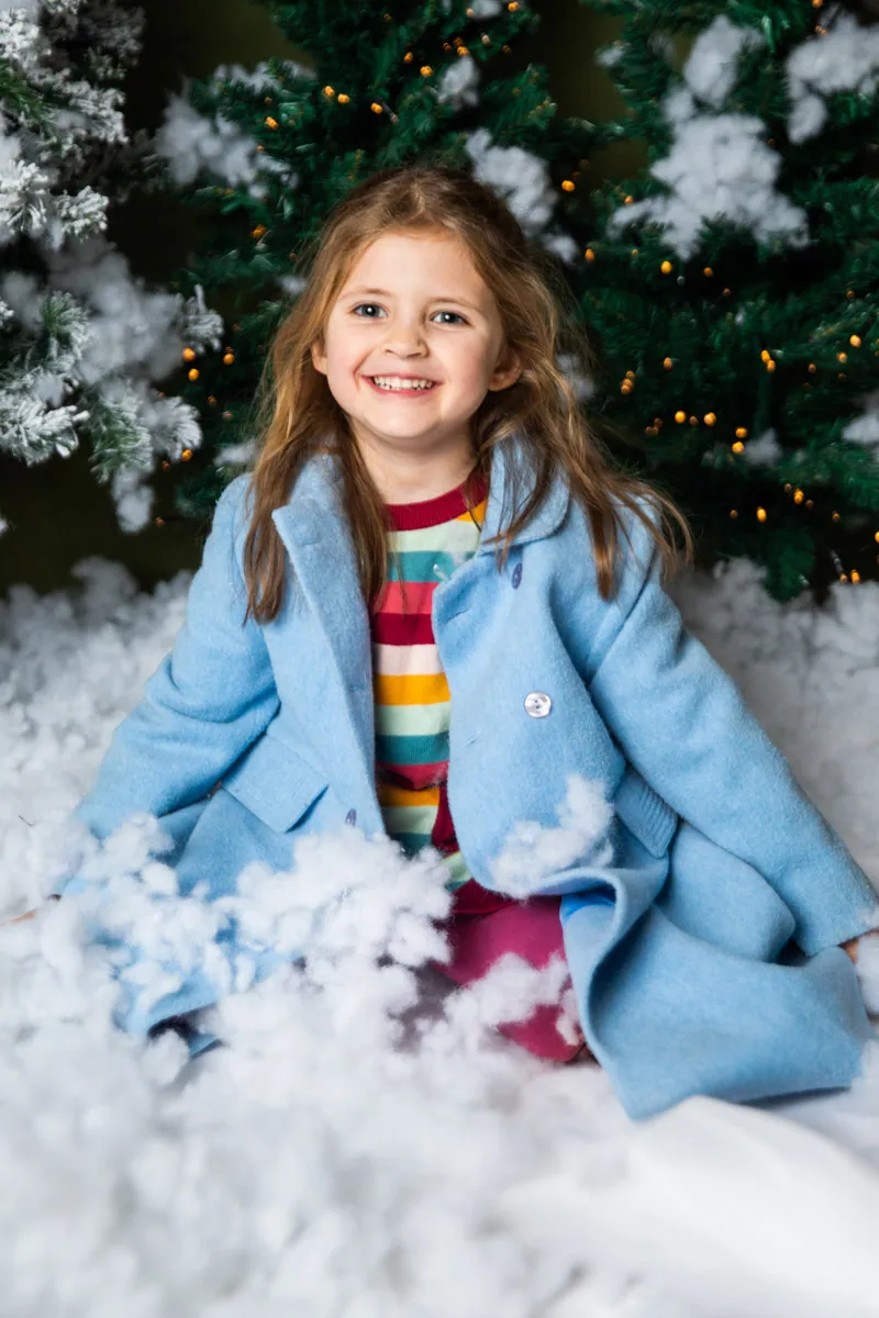 Mädchen im blauen Mantel vor verschneitem Winterhintergrund.